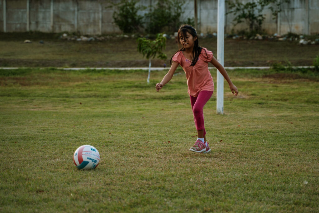 Young girl running on a grass field toward a ball, about to kick